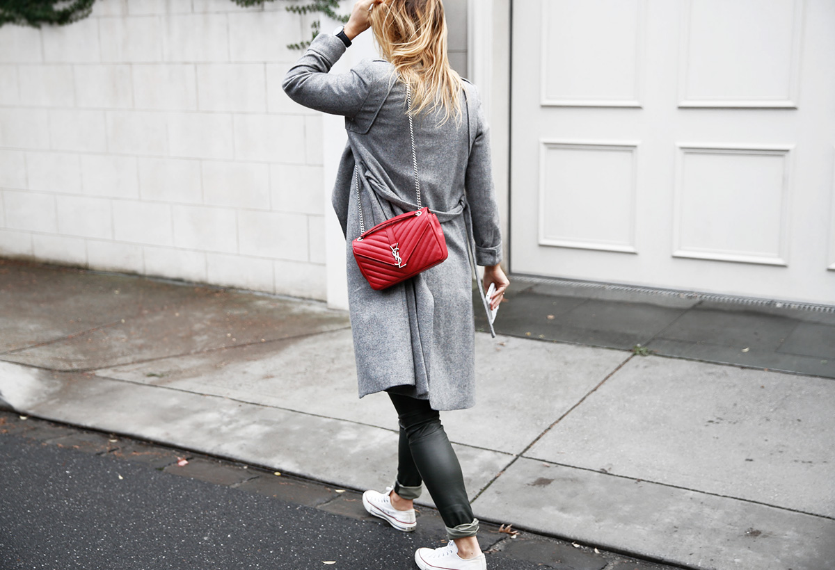 walking in grey coat in leather leggings with red ysl bag